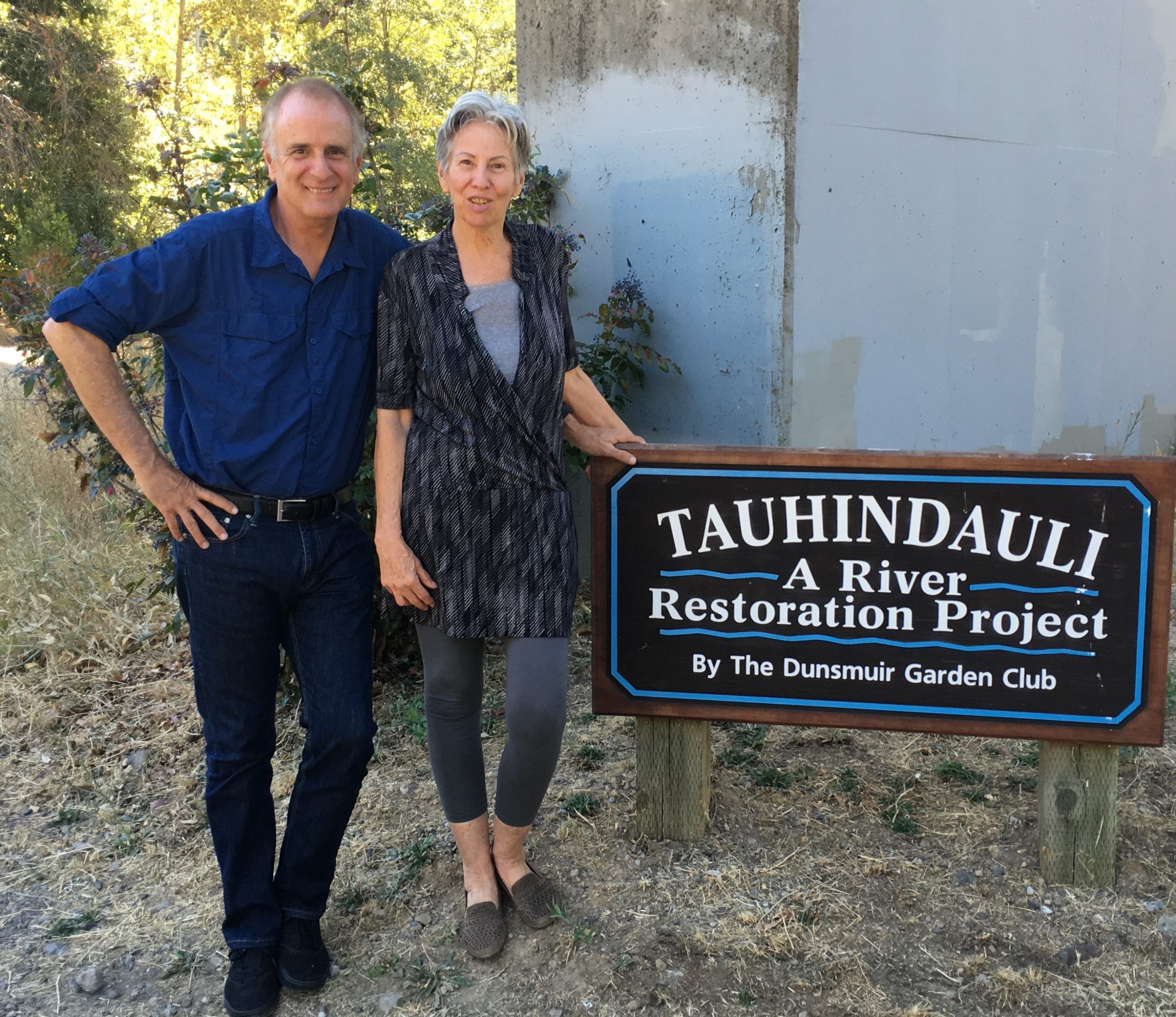 Tour Guide Angel Gomez standing next to a woman and sign that reads Tauhindauli Park, A River Restoration Project by The Dunsmuir Garden Club