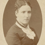 Sepia photo of a woman with dark hair, light skin and a dark dress.