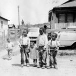 Five Black children standing in front of a home and driveway.