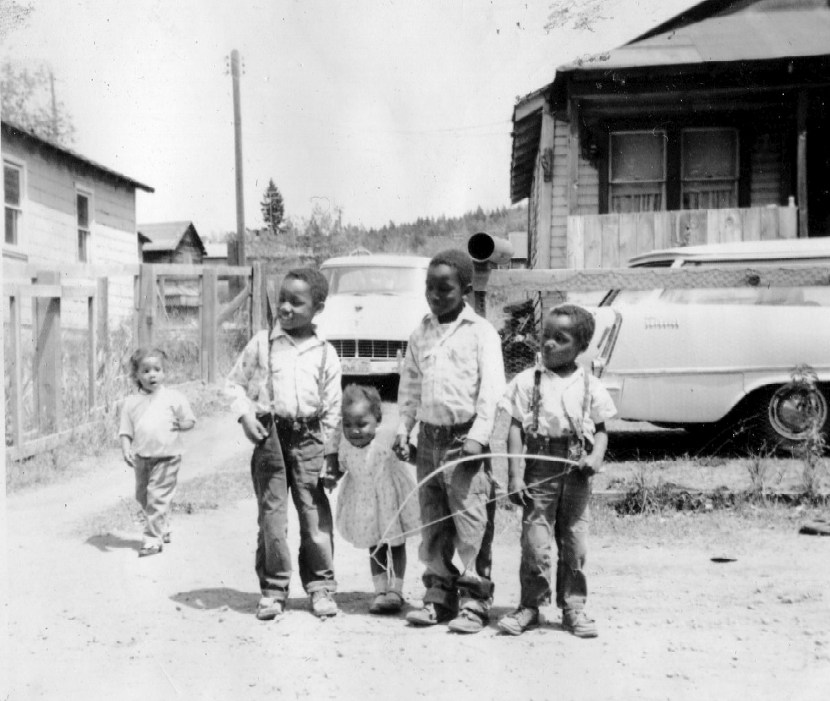 Five Black children standing in front of a home and driveway.